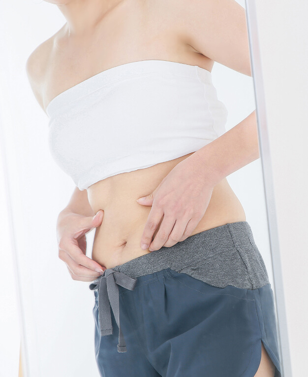 Liposuction woman in front of mirror pinching her midsection
